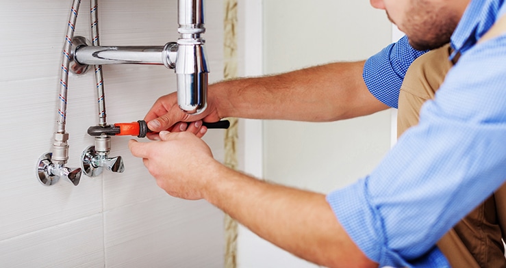 Plumber tightening water valves on a bathroom sink.